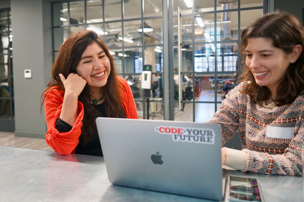 Two women smiling and using a laptop together